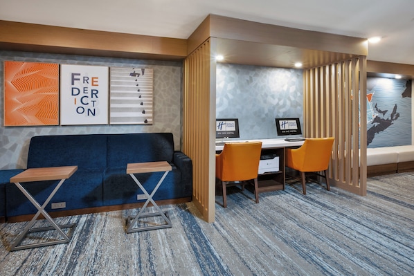 A hotel room with a blue sofa, two chairs, a desk with a computer, and a large window with a view.