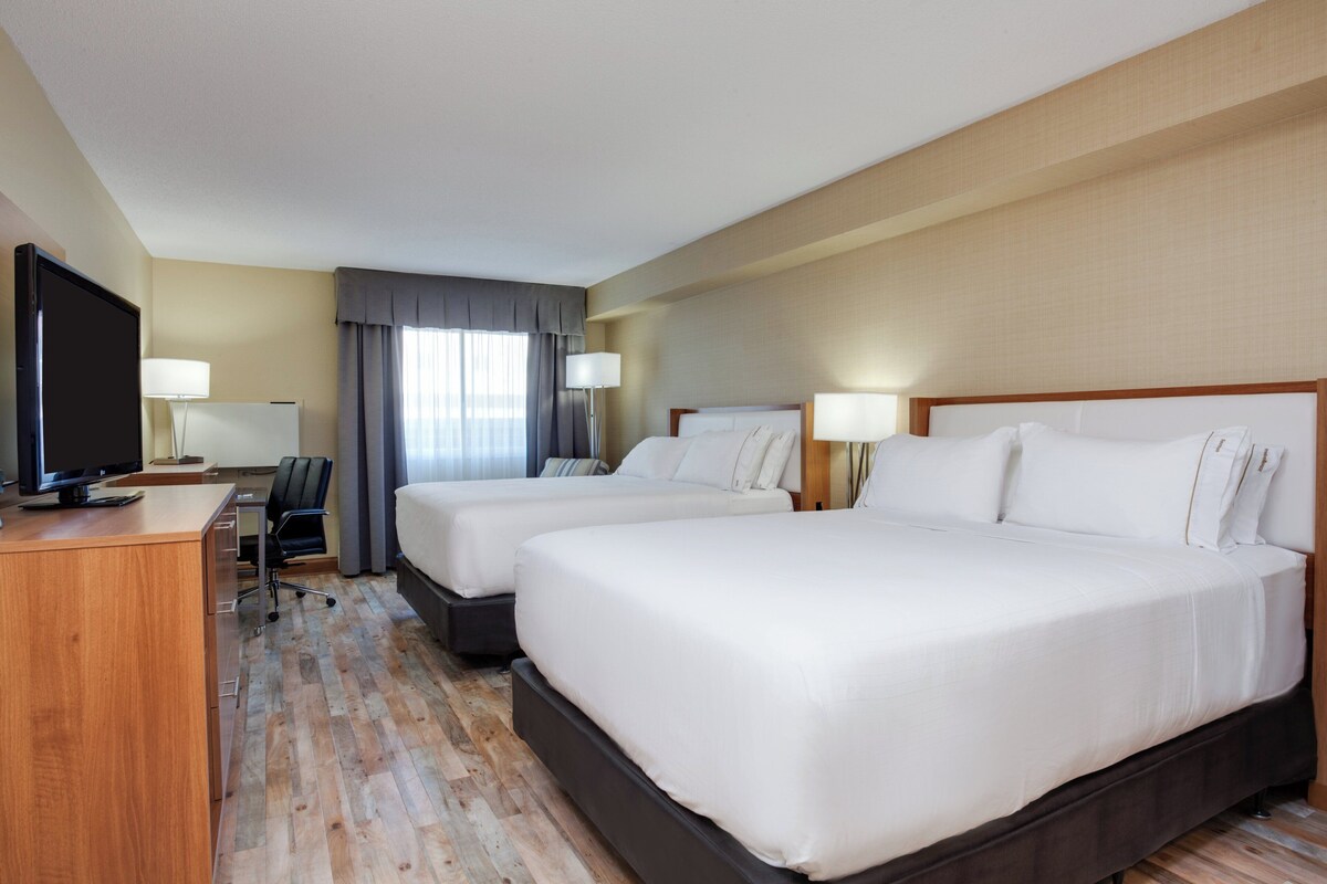 Quarto de hotel com duas camas, uma escrivaninha com televisão e uma cadeira.