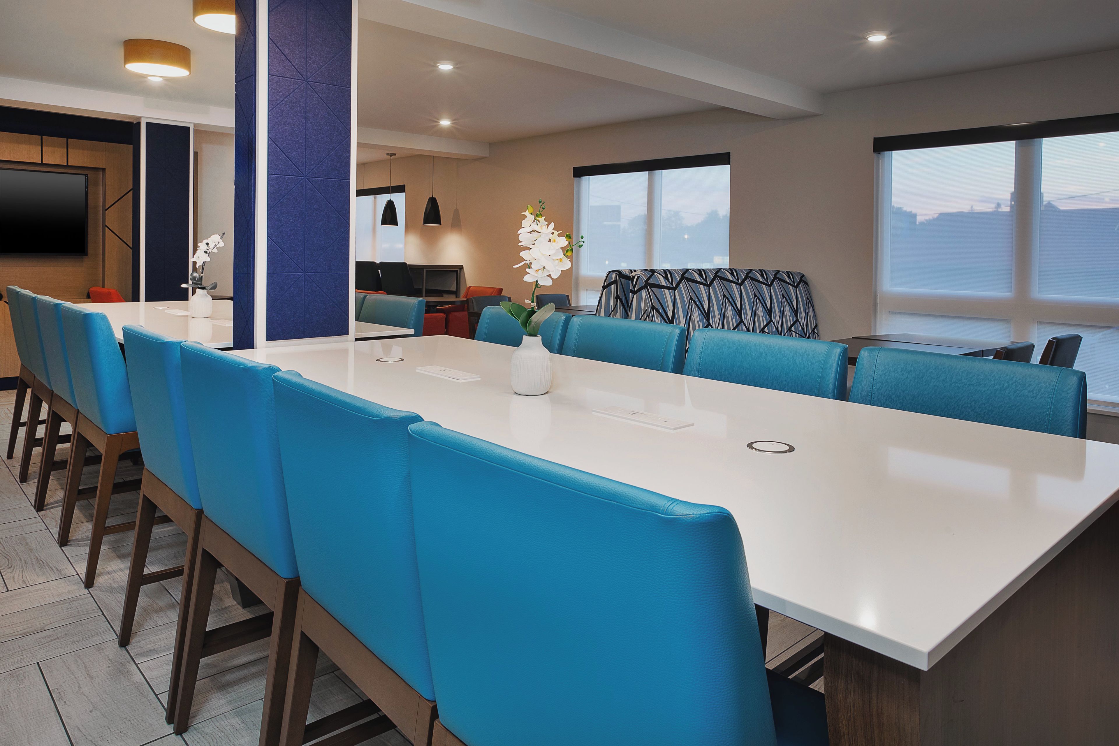 Una sala de conferencias moderna con una mesa larga y sillas azules, un televisor de pantalla plana y un amplio ventanal con vistas.