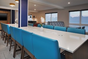 A modern conference room with a long table and blue chairs, a flat-screen TV, and a large window with a view.