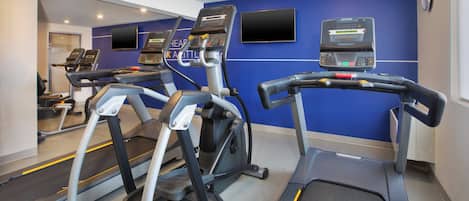 A gym with treadmills, stationary bikes, and a mirrored wall.