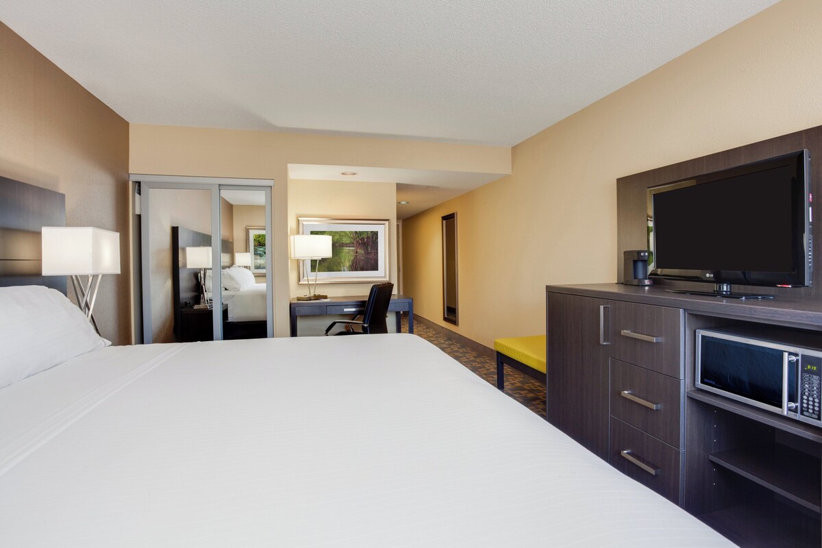Ein Hotelzimmer mit einem großen Bett, einem Schreibtisch mit Stuhl, einem Fernseher und einer Mikrowelle.
