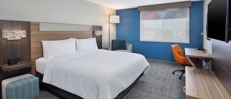 Una habitación de hotel con cama, escritorio, silla, televisor y ventana.