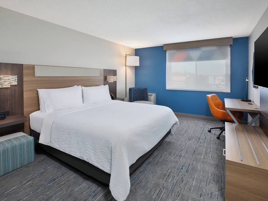 A hotel room with a bed, a desk, a chair, a TV, and a window.