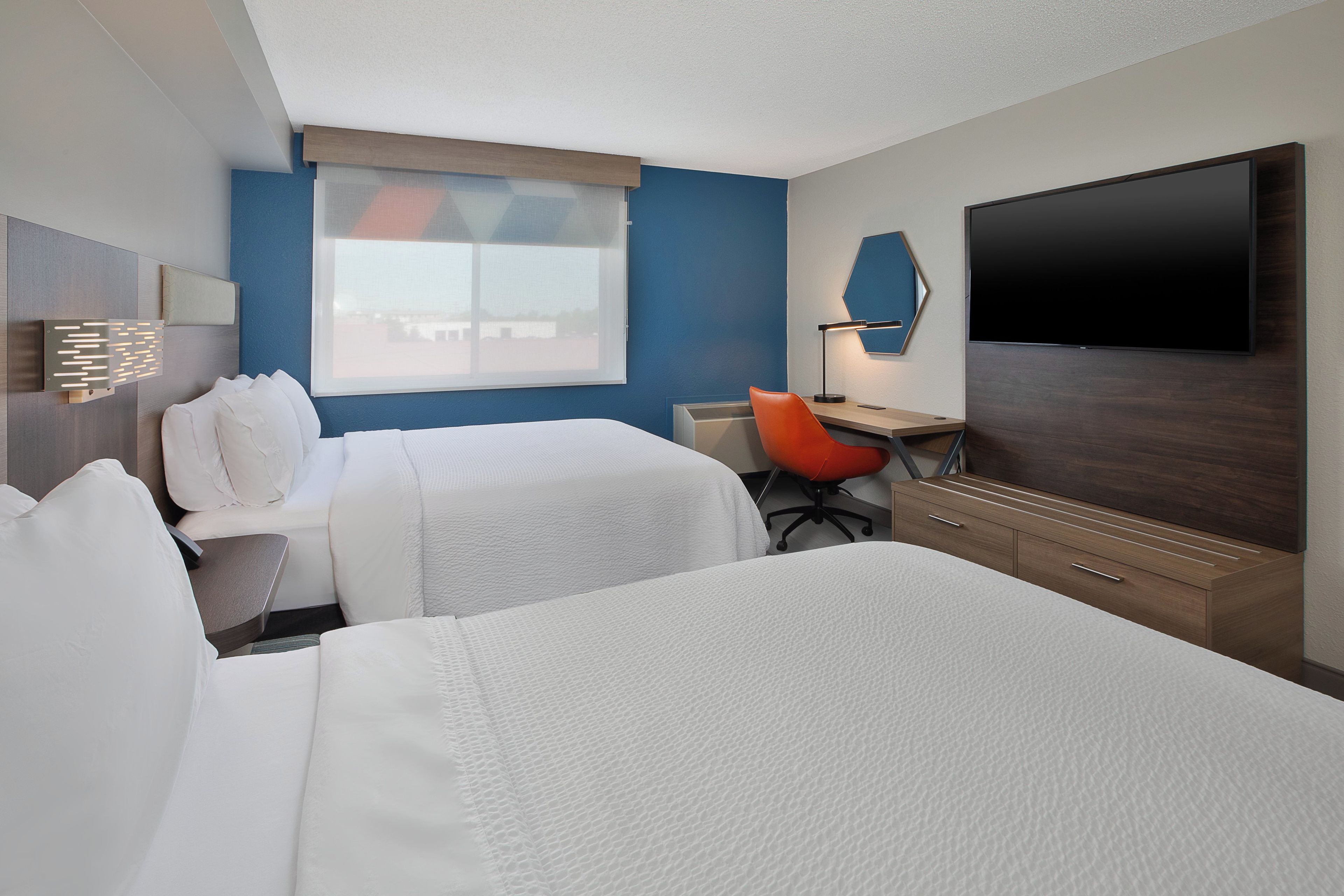 Ein Hotelzimmer mit zwei Betten, einem Schreibtisch, einem Sessel, einem Flachbildfernseher und einem Fenster mit Blick.