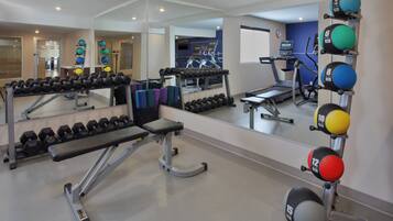 Une salle de sport équipée de machines d’exercice, de miroirs et d’un tapis de course.