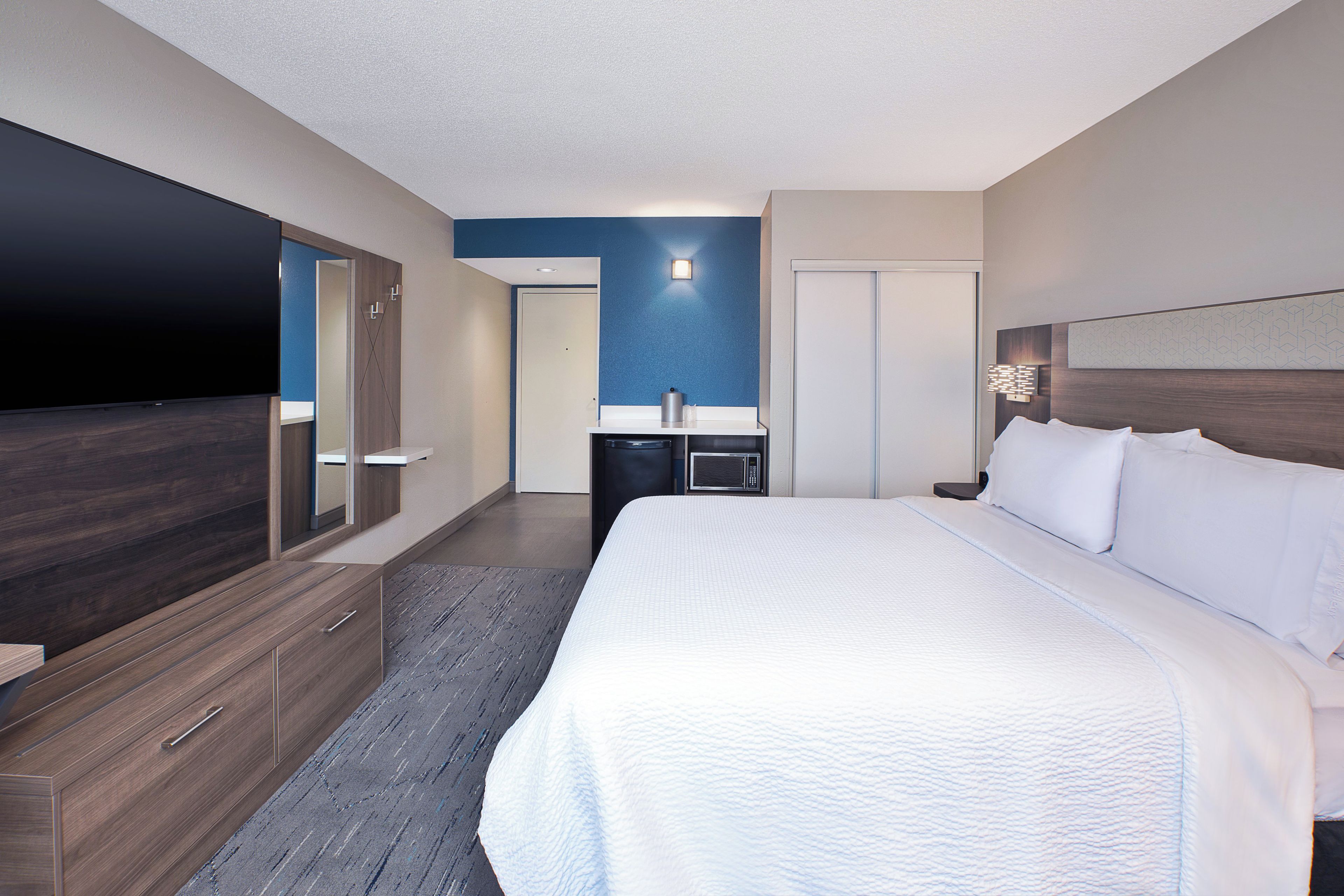 Een hotelkamer met een groot bed, een flatscreen televisie, een minibar en een badkamer die door een open deur zichtbaar is.