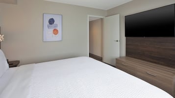A hotel room with a bed, a flat-screen TV, a wooden dresser, and a door leading to a hallway.