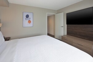 A hotel room with a bed, a flat-screen TV, a wooden dresser, and a door leading to a hallway.