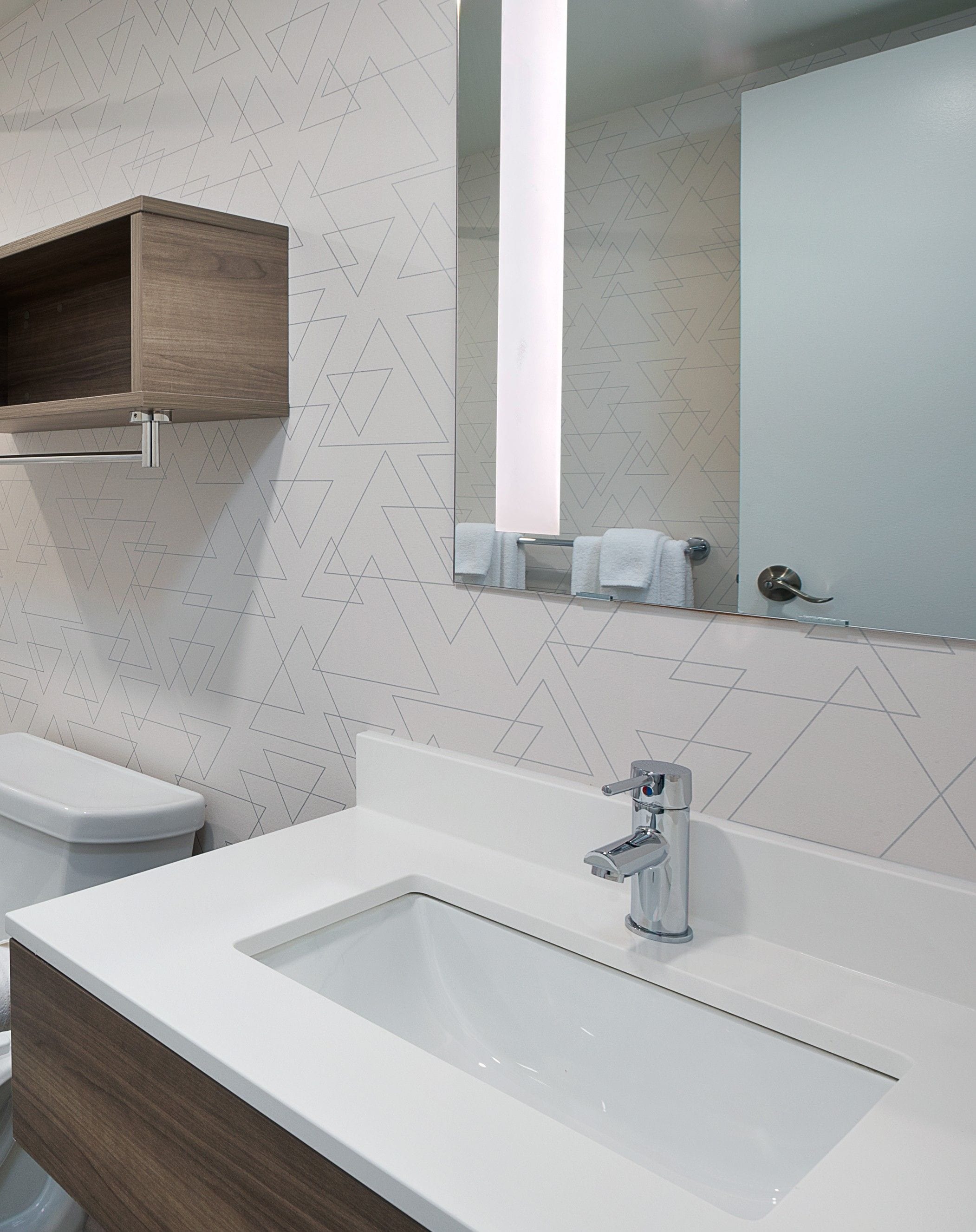 A modern bathroom with a white sink, a mirror, and a wooden cabinet.