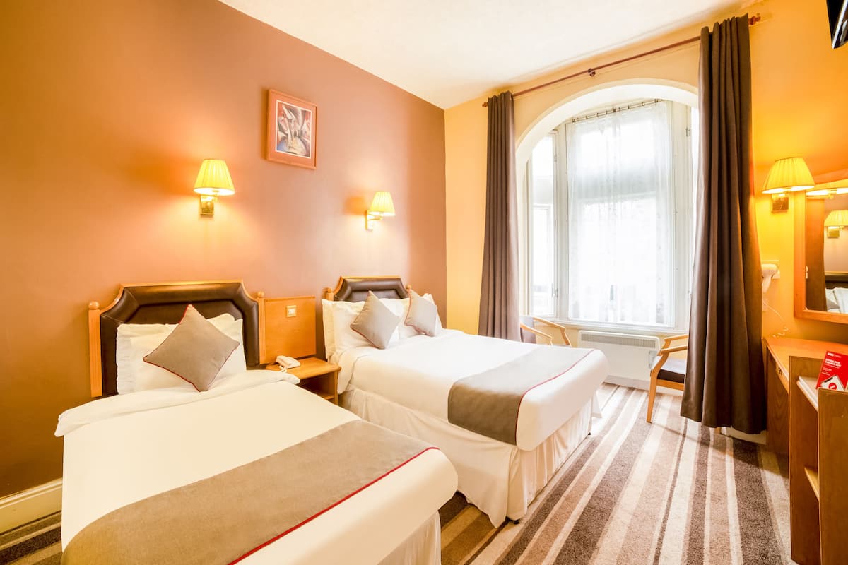 A hotel room with two beds, a desk, a chair, and a large window with curtains.