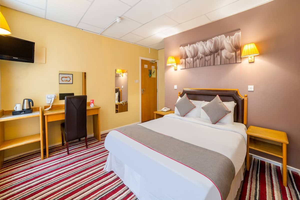 A hotel room with a bed, desk, chair, and a television.