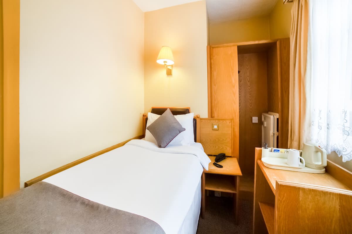 A hotel room with a bed, bedside table, lamp, and a wooden wardrobe.