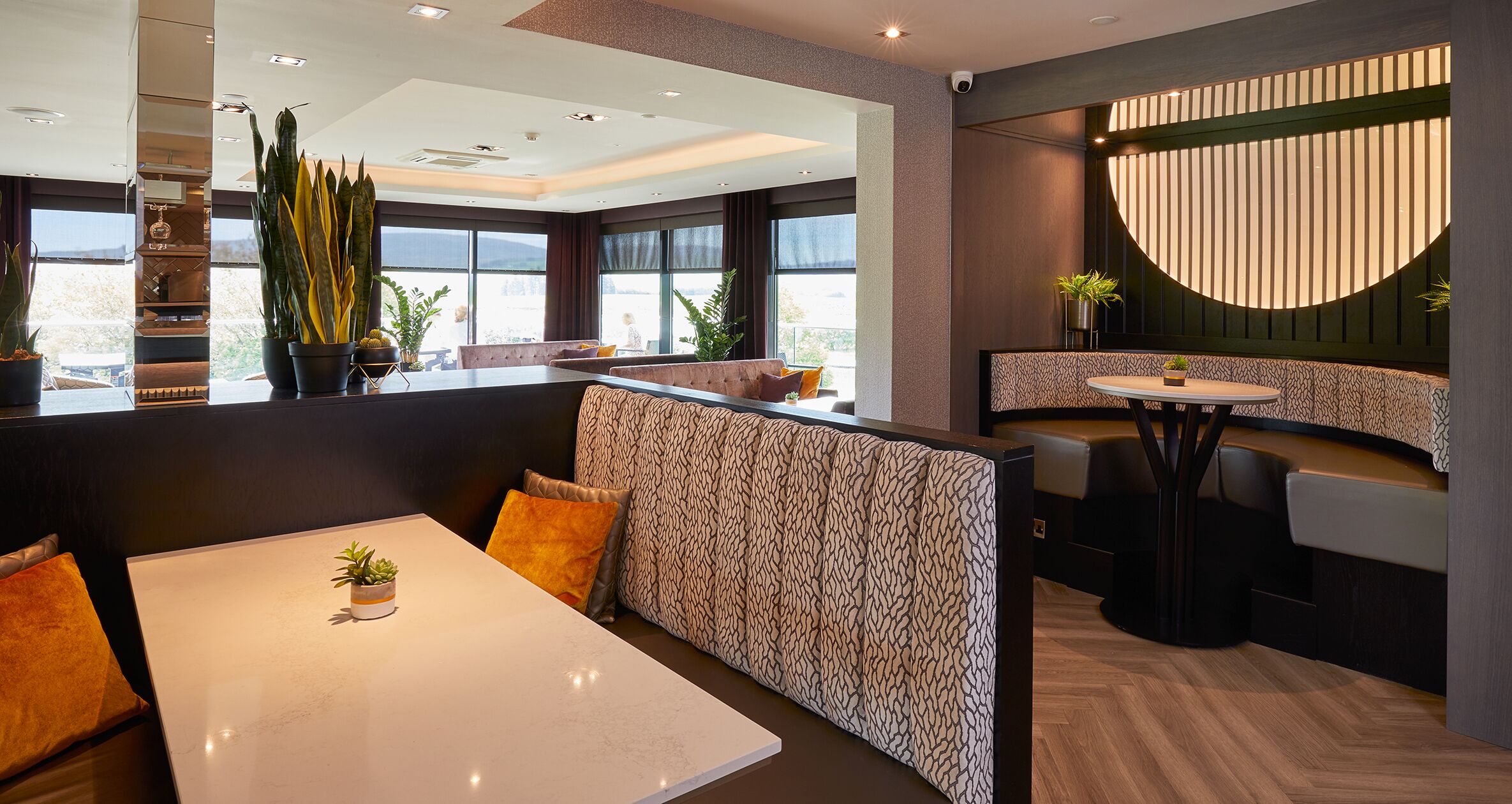 A modern restaurant interior with high-backed booths, a central dining table, and a curved seating area.