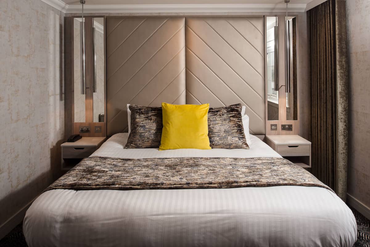 A hotel room with a large bed, a headboard with a geometric pattern, bedside tables with lamps, and a mirror.