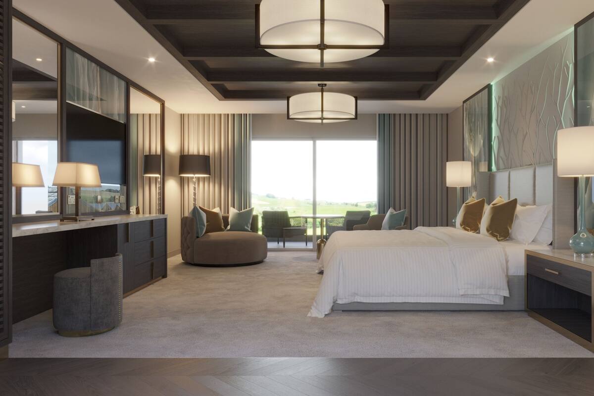 A modern hotel room with a large bed, a desk with a computer, a sofa, and a view of the outdoors.