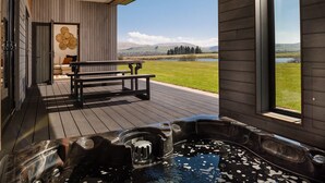 A hot tub on a wooden deck with a view of a lake and mountains.