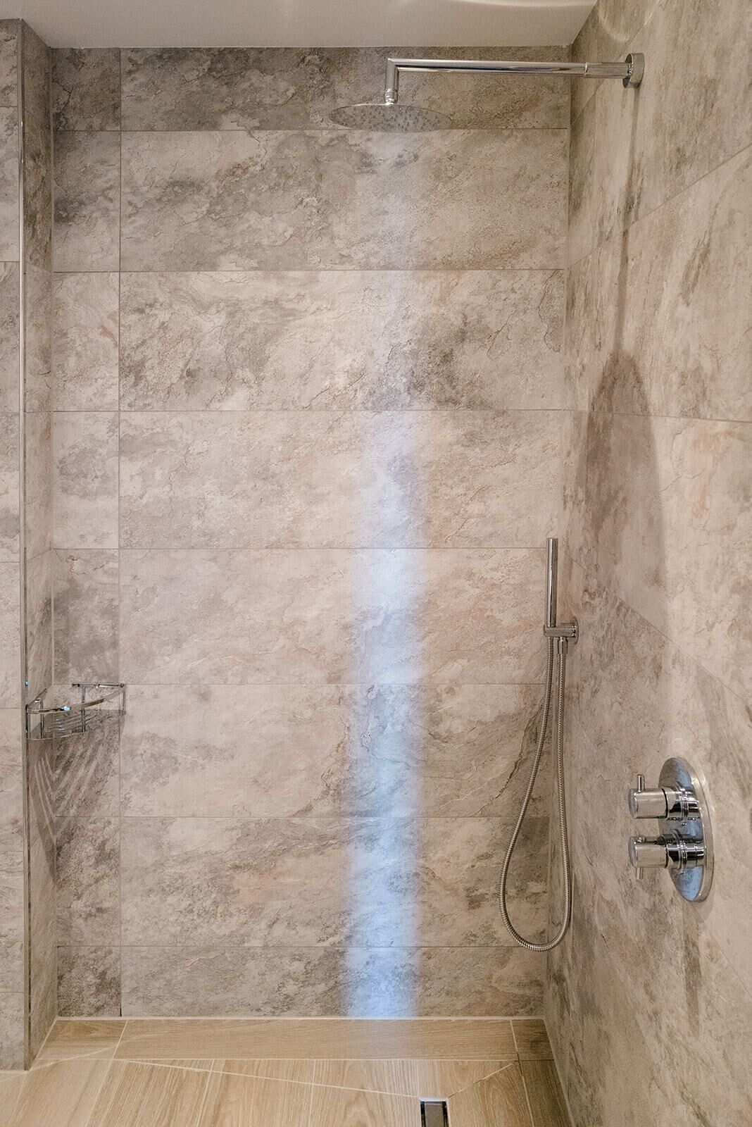 Ducha a pie con puerta de cristal, cabezal de ducha de mano y grifo empotrado.