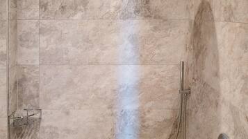 Ducha a pie con puerta de cristal, cabezal de ducha de mano y grifo empotrado.