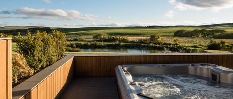 A hot tub on a wooden deck overlooking a lake and rolling hills.