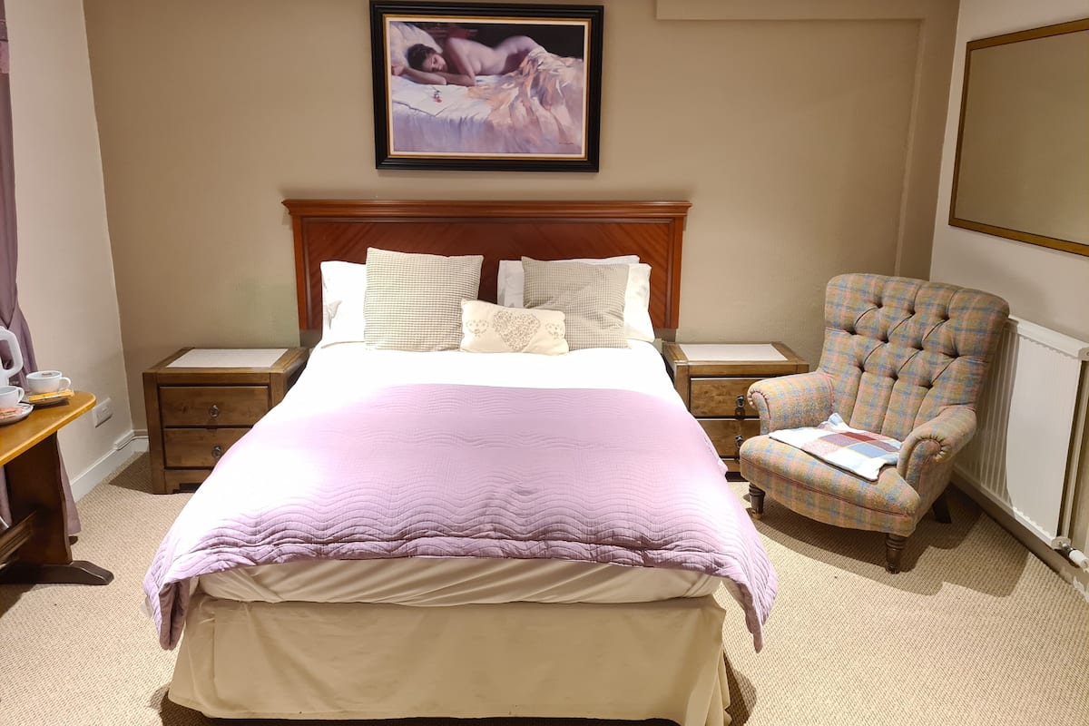 A hotel room with a large bed, a wooden headboard, a chair, a nightstand, and a framed picture on the wall.