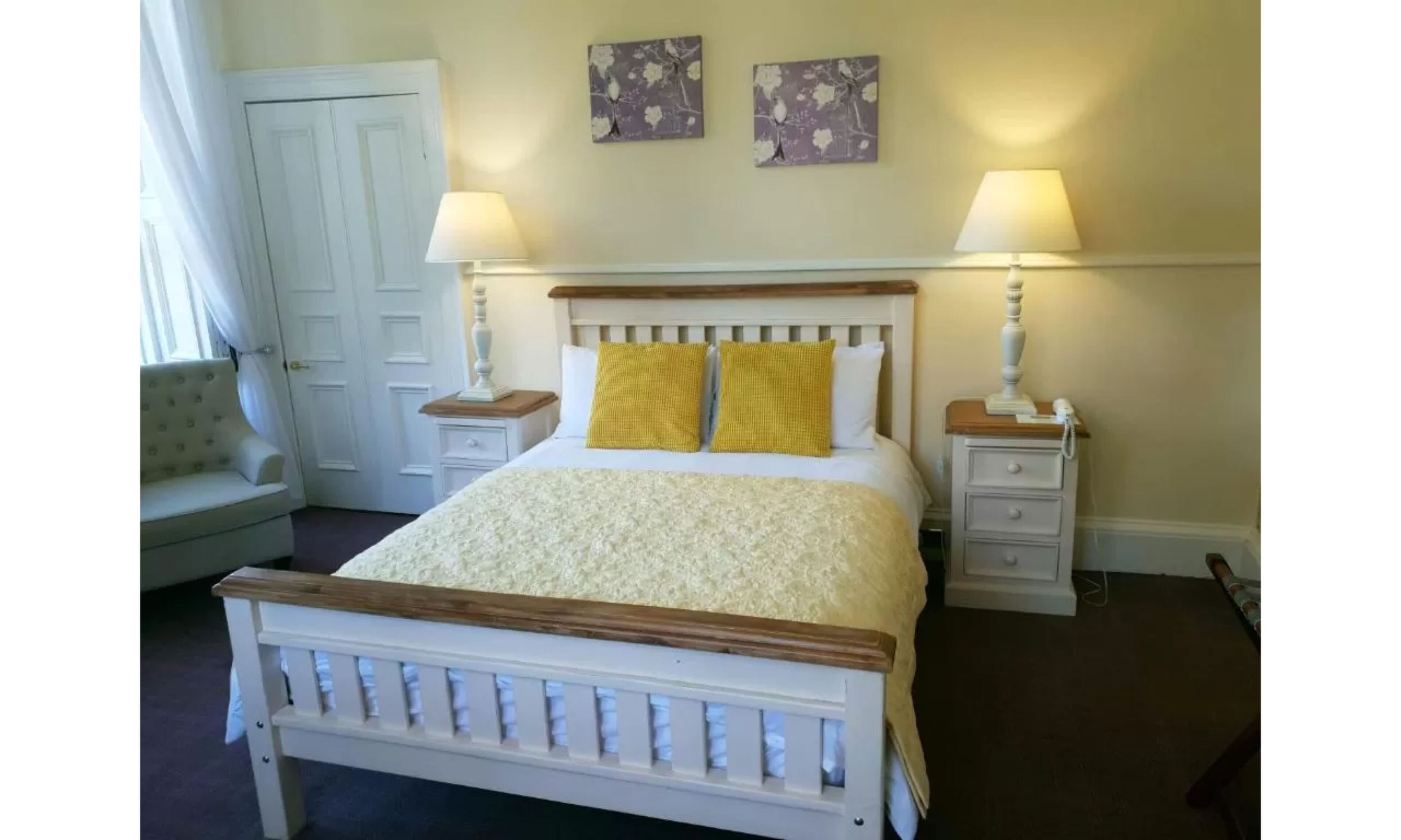 Une chambre à coucher bien rangée, avec un lit, deux tables de chevet, une chaise et deux tableaux accrochés au mur.