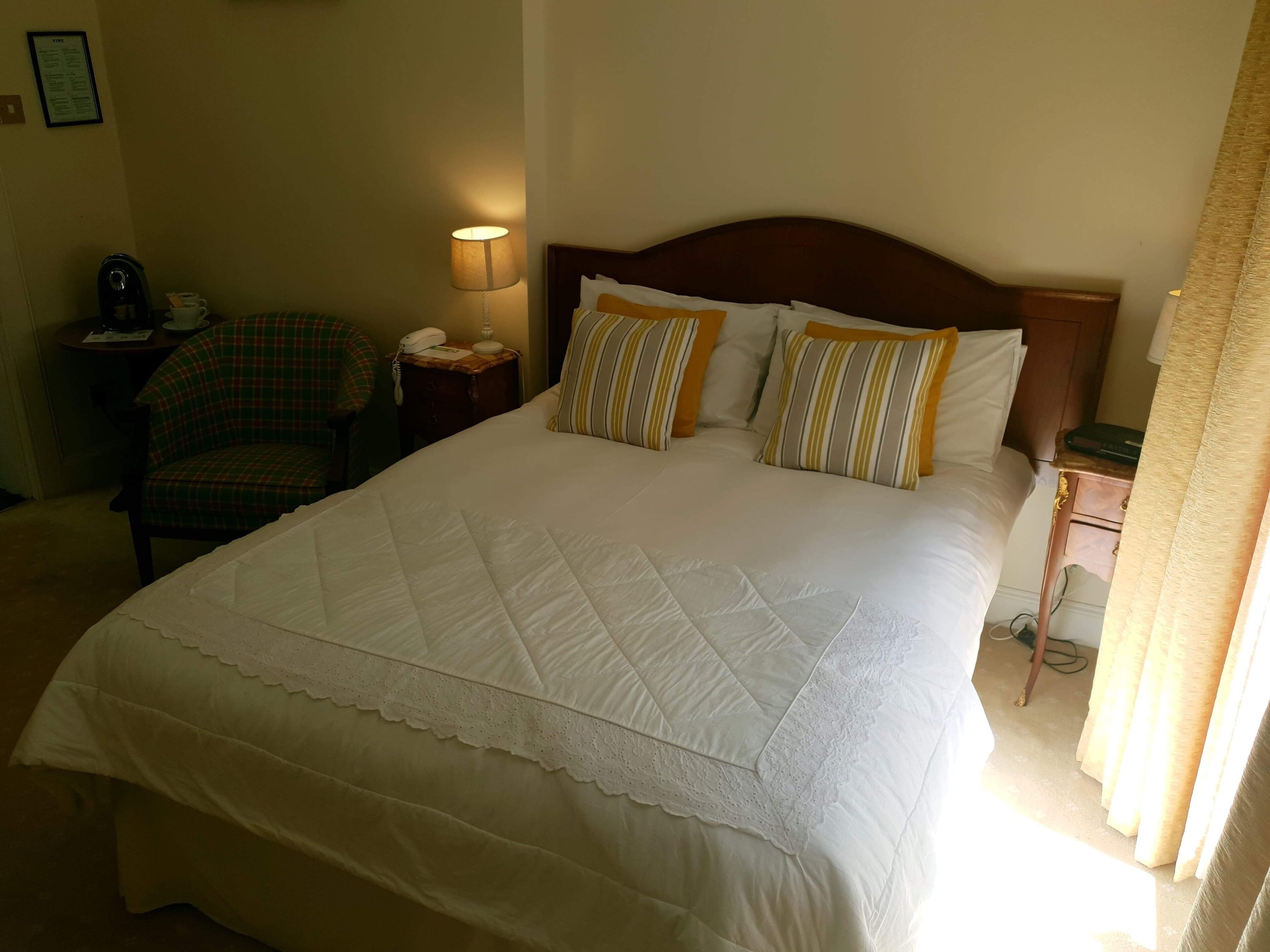 Una habitación de hotel con una cama grande, una silla, una mesita de noche con lámpara y una pequeña mesa con teléfono.