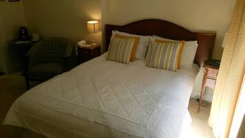 Una habitación de hotel con una cama grande, una silla, una mesita de noche con lámpara y una pequeña mesa con teléfono.