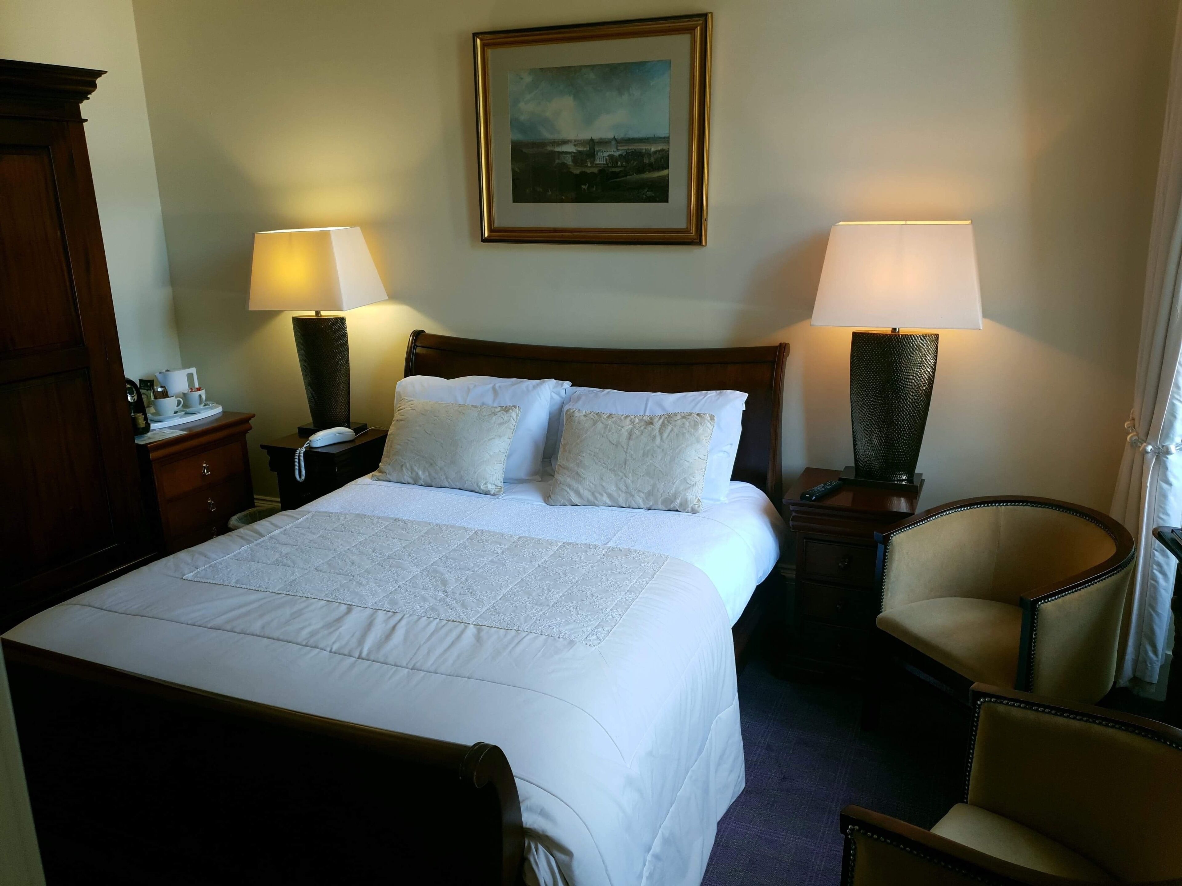 Ett hotellrum med en stor säng, två sänglampor, en stol och en tavla på väggen.