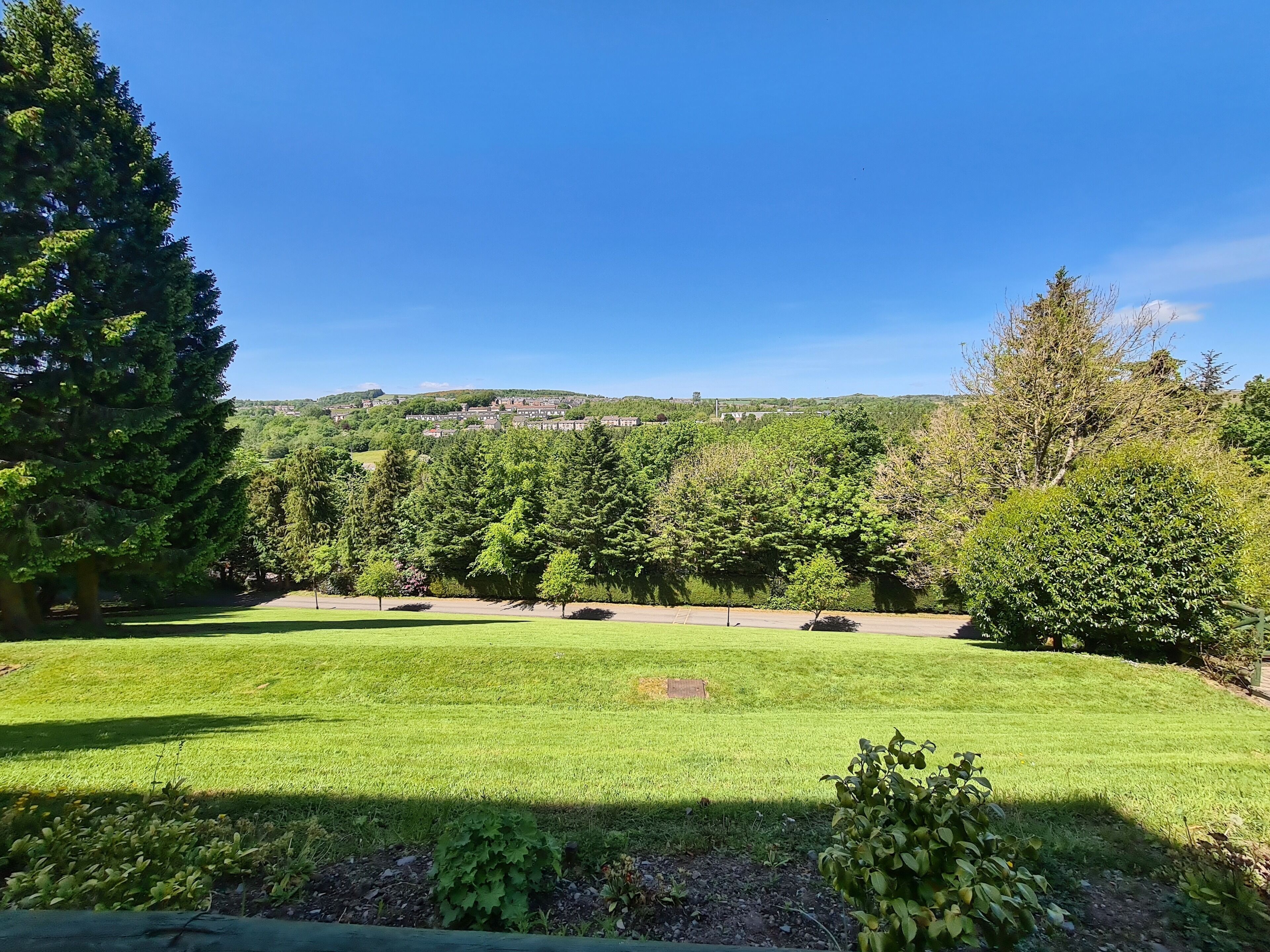 A well-maintained grassy area with trees and a distant view of a town on a hill.
