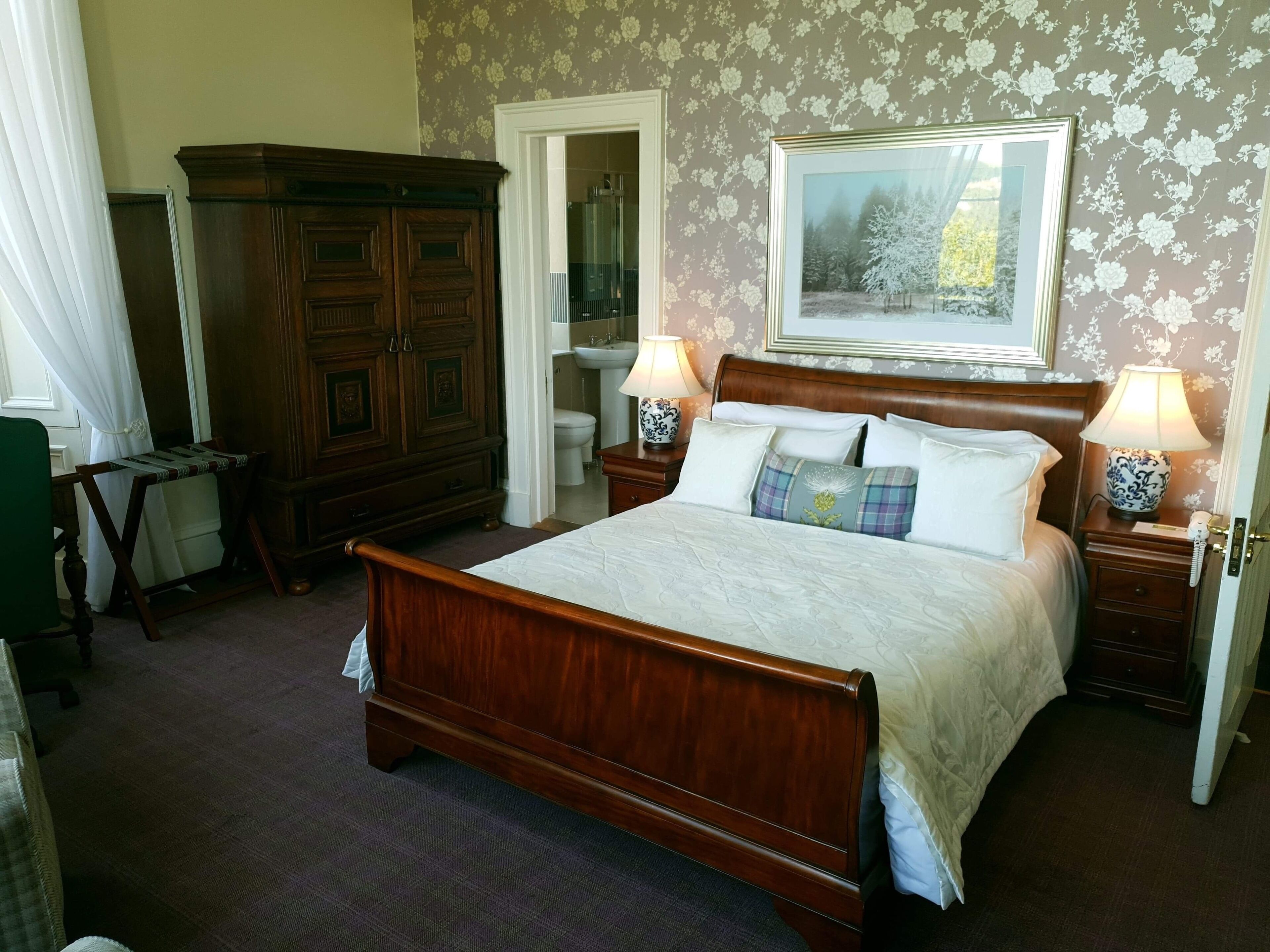 A bedroom with a wooden bed, two bedside tables with lamps, a dresser, a mirror, and a framed picture on the wall.
