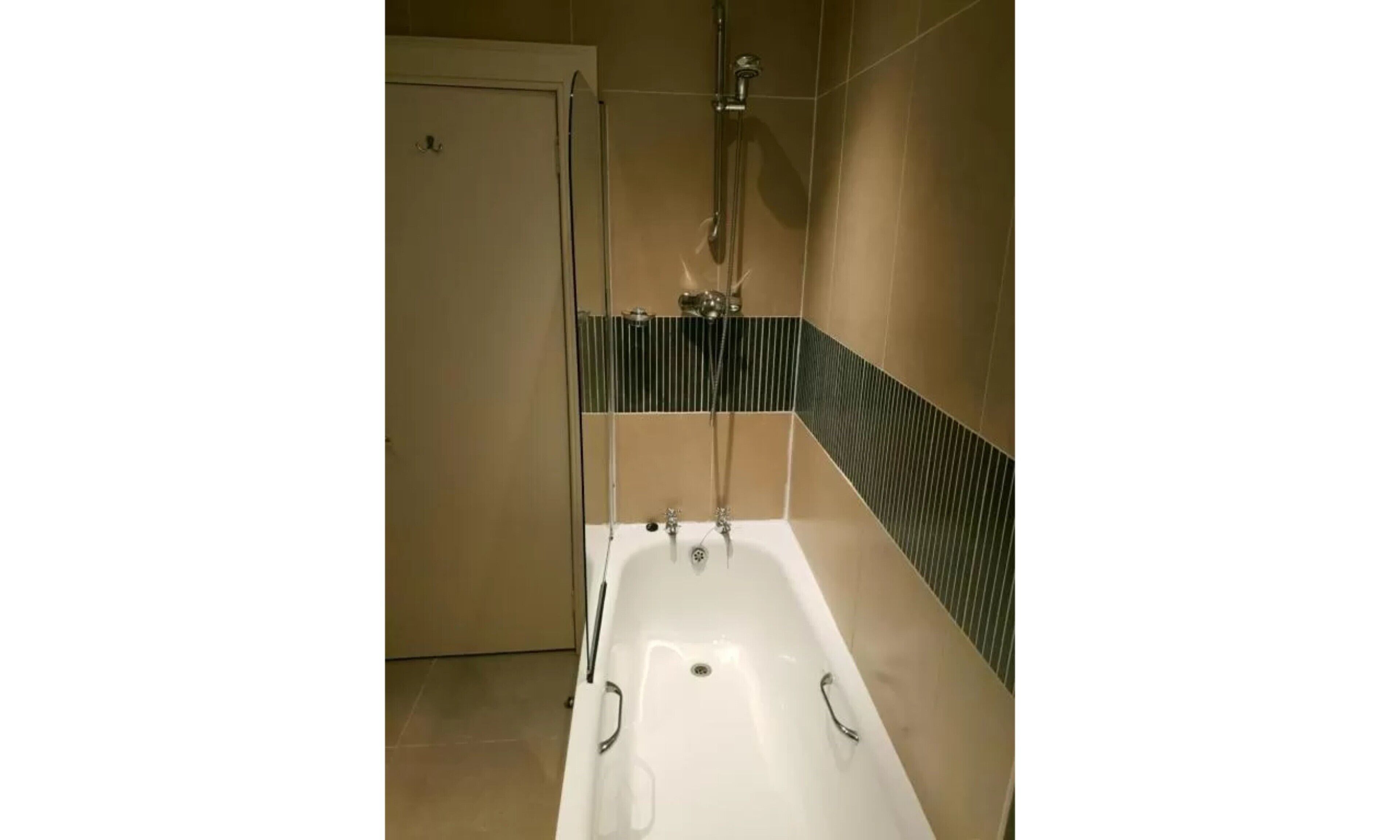 Et badeværelse med badekar, bruser og dør.