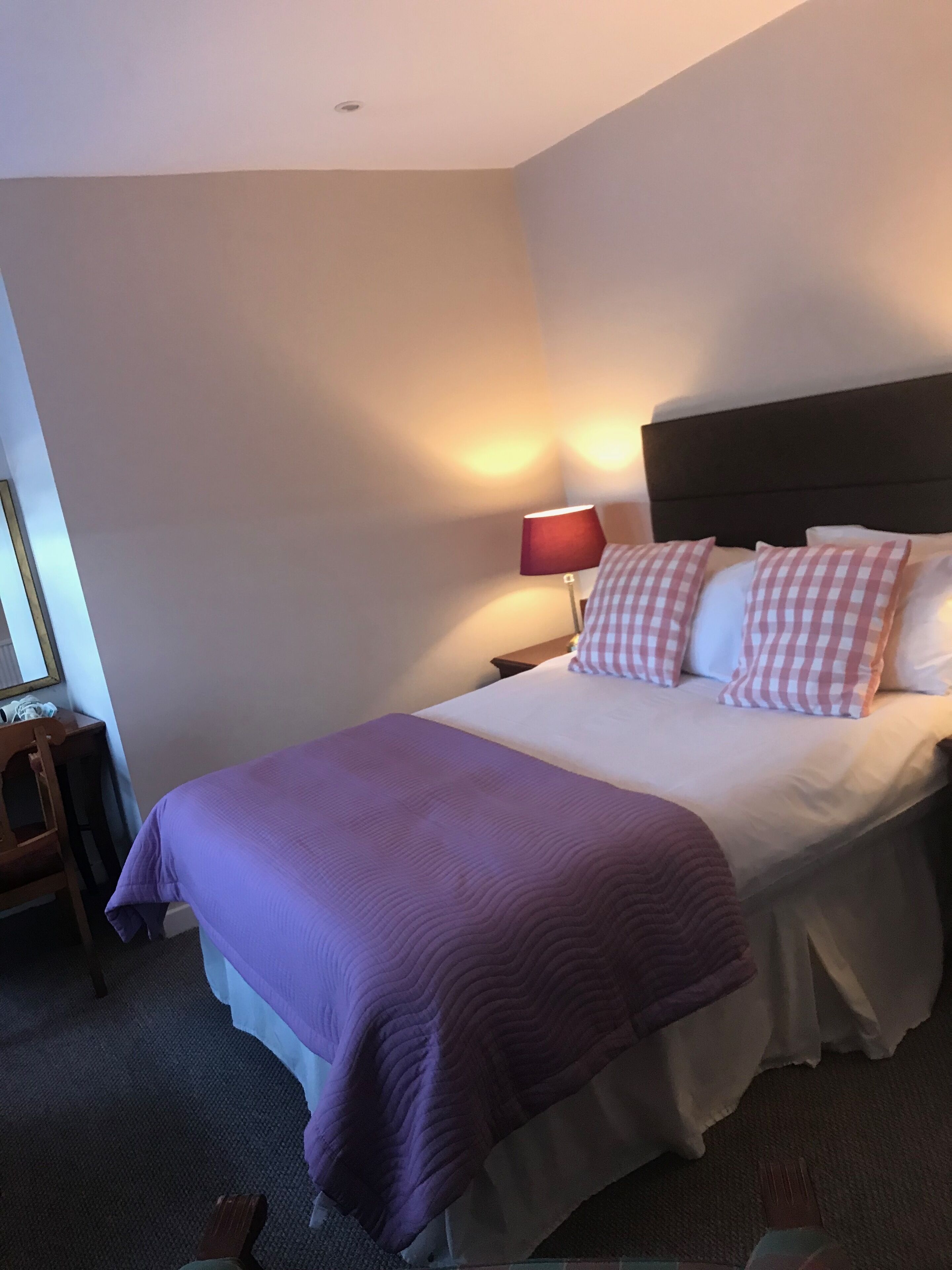 A hotel room with a bed, a nightstand, a lamp, and a chair.