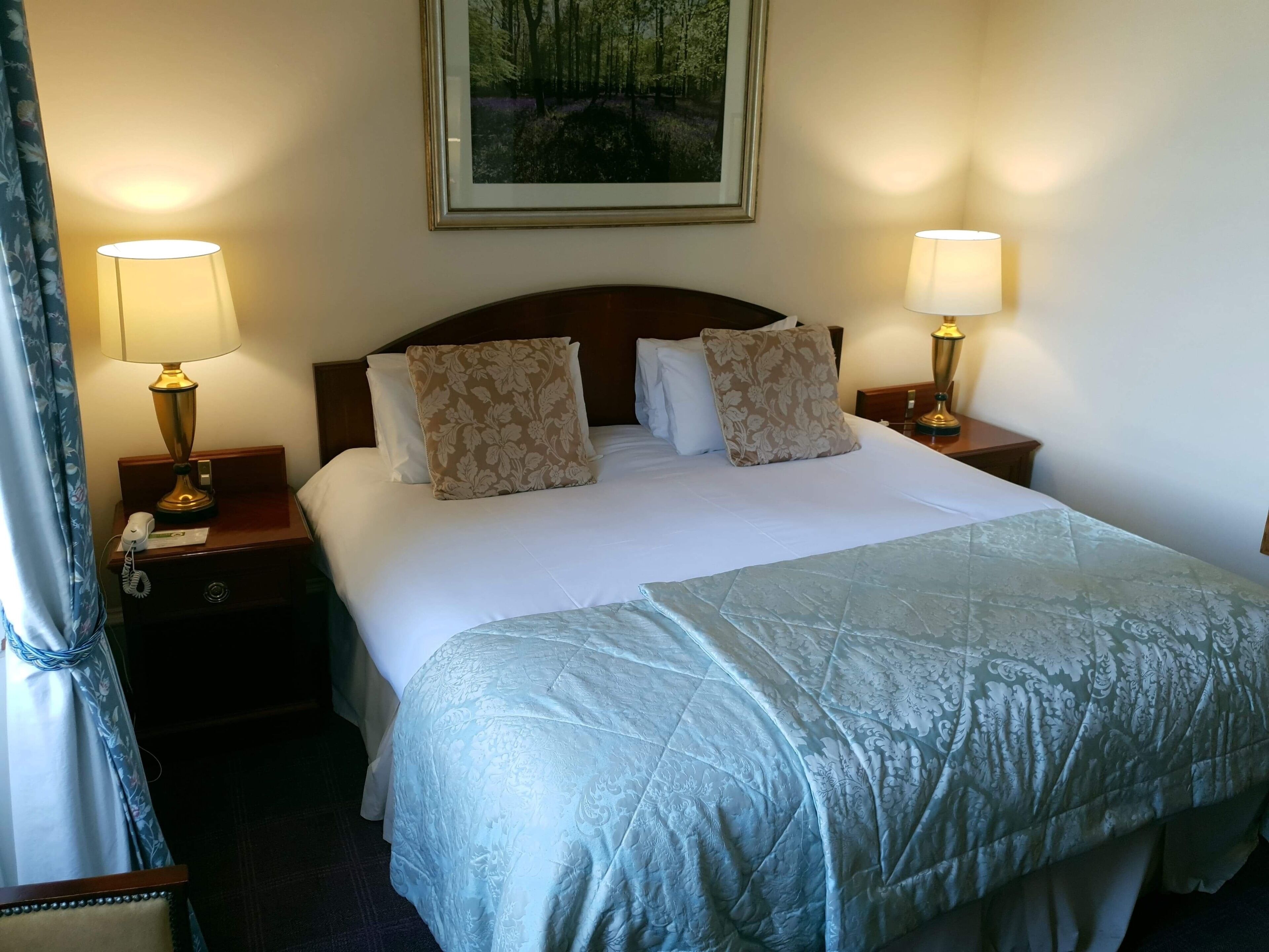 Una habitación de hotel con una cama grande, dos lámparas de noche, un teléfono y un cuadro en la pared.