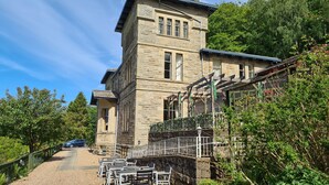 A stone building with a balcony, surrounded by greenery and a gravel path with outdoor seating. - Mansfield House Hotel (Hawick)