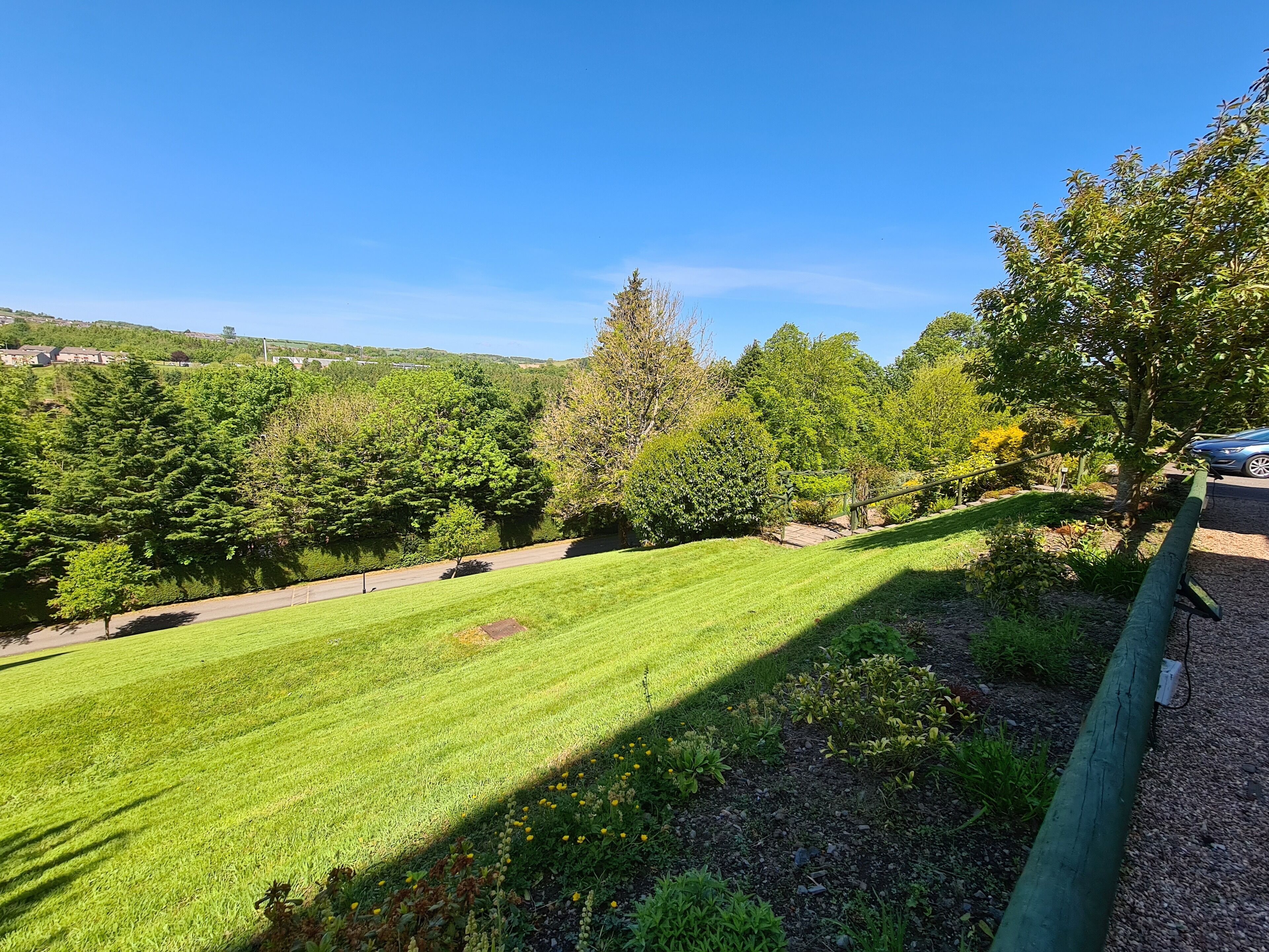 A well-maintained grassy area with a paved path, surrounded by trees and a clear blue sky.