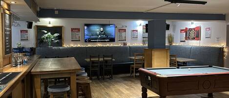 A bar area with a pool table, bar stools, and a television screen.