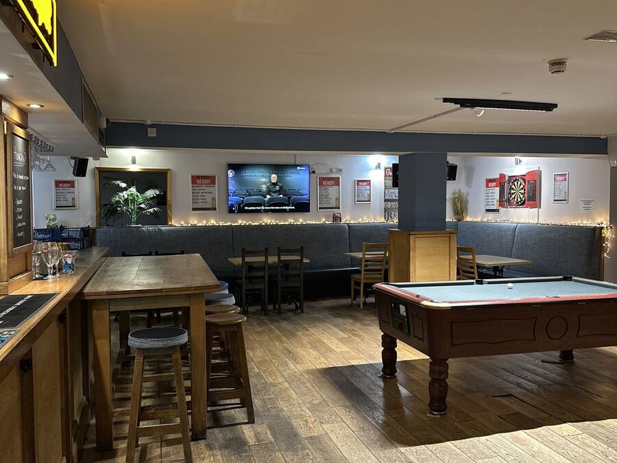 A bar area with a pool table, bar stools, and a television screen.