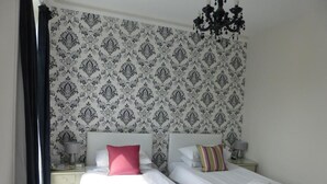 A double bed with a striped bedspread, a nightstand with a lamp, and a patterned wallpaper. - Harry's Hotel (Aberystwyth)