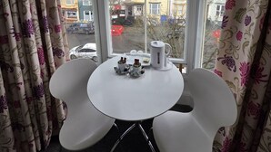 A room with a bay window, two white chairs, a small table with a tray, and floral curtains. - Harry's Hotel (Aberystwyth)
