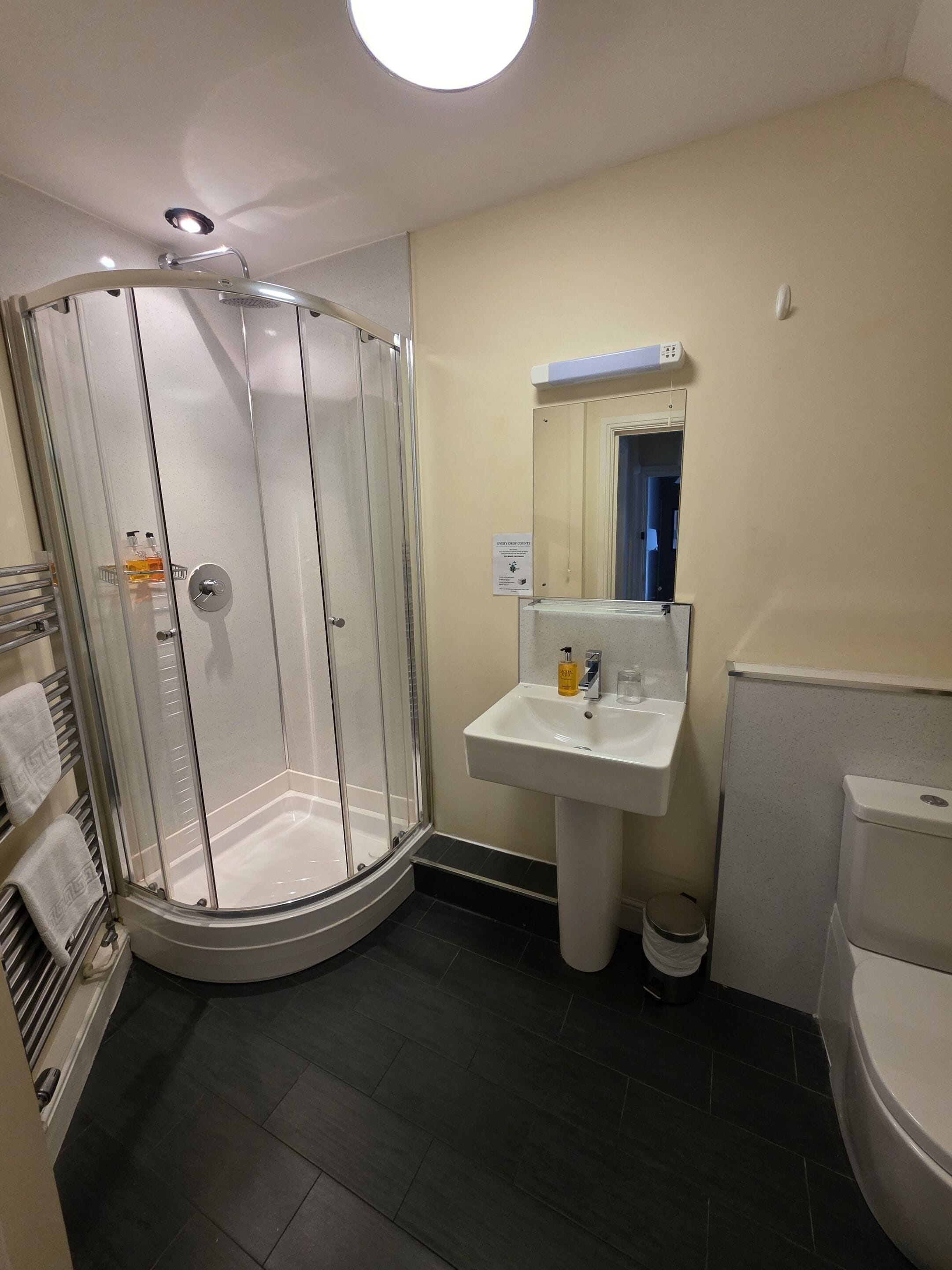 Un baño con ducha de vidrio, lavamanos con espejo y retrete.