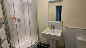 Un baño con ducha de vidrio, lavamanos con espejo y retrete.