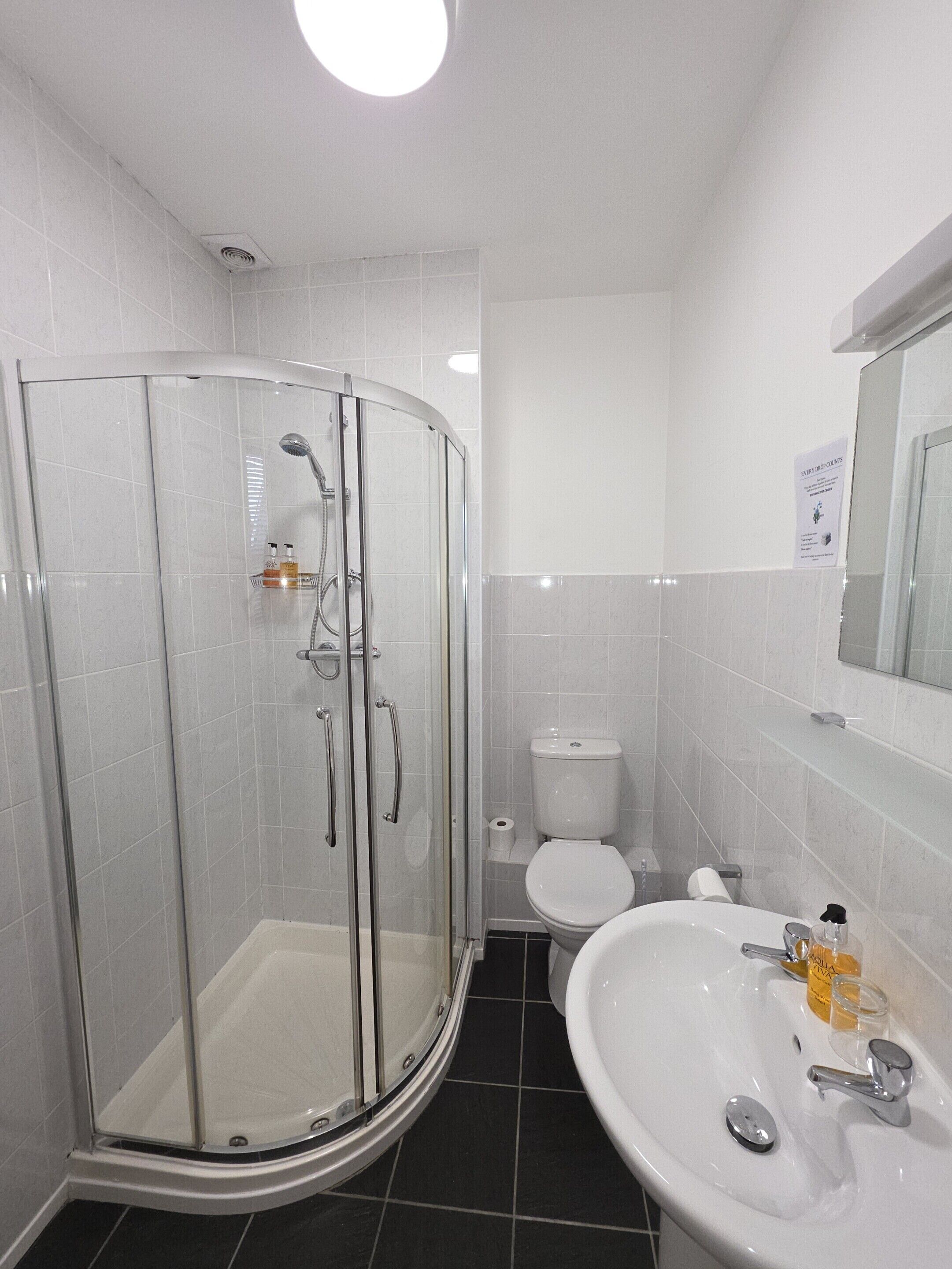 Un baño moderno con ducha de vidrio, un lavamanos blanco y un inodoro.