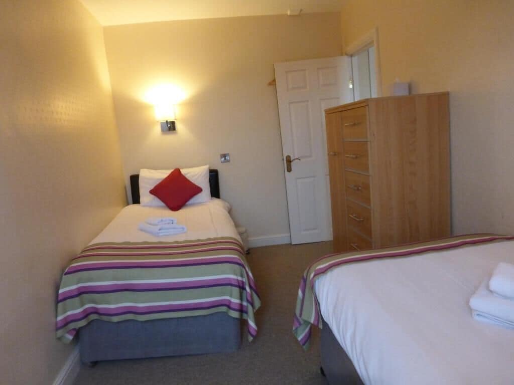 A bedroom with two beds, a wardrobe, and a wall-mounted light.