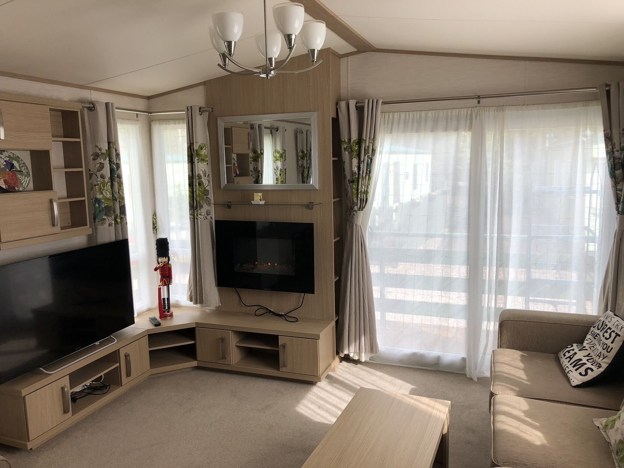 Un salón moderno con televisor de pantalla plana, muebles de madera, un sofá con cojín y una lámpara de araña.
