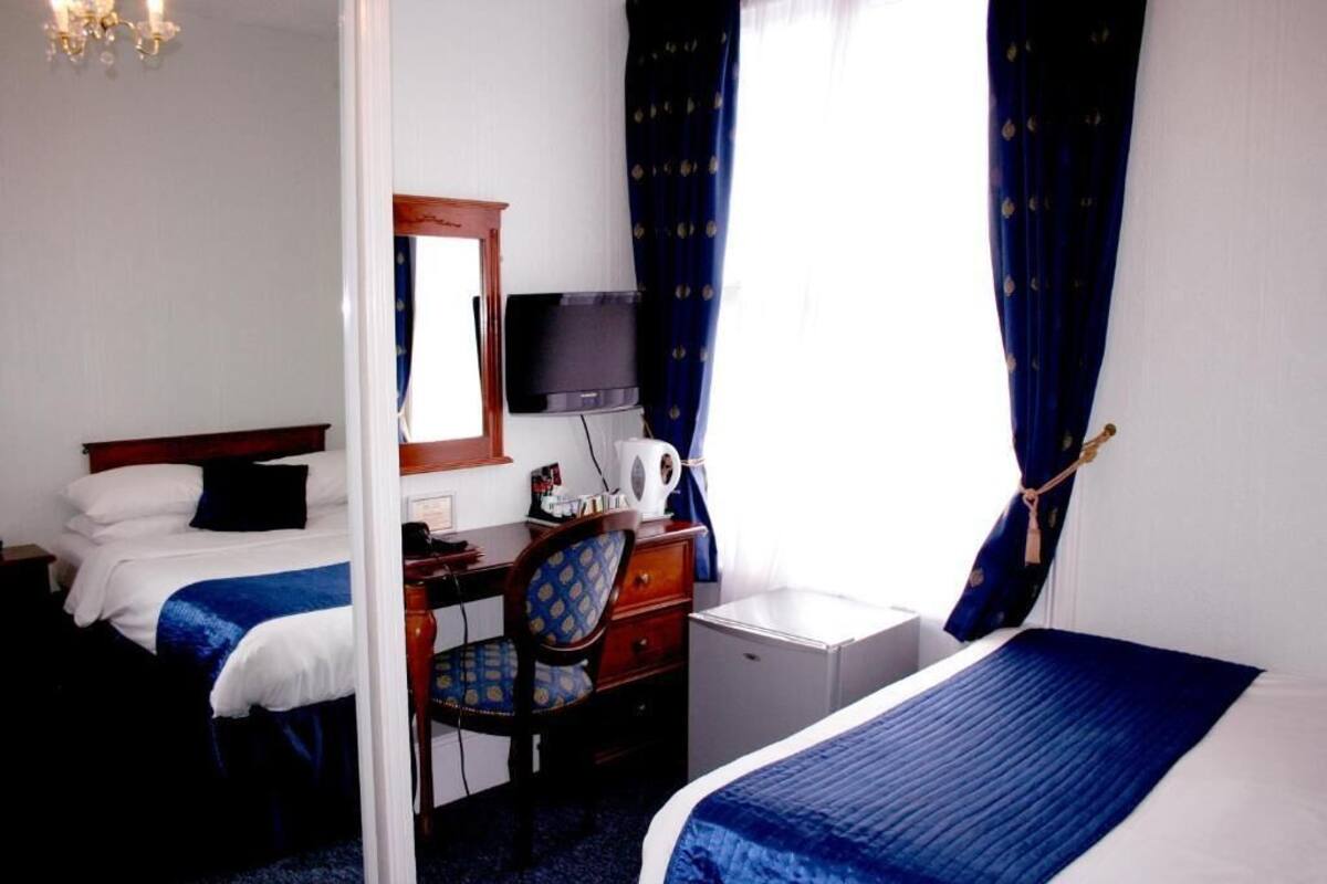 Een hotelkamer met een bed, een bureau, een stoel, een televisie en een klein wit kastje.