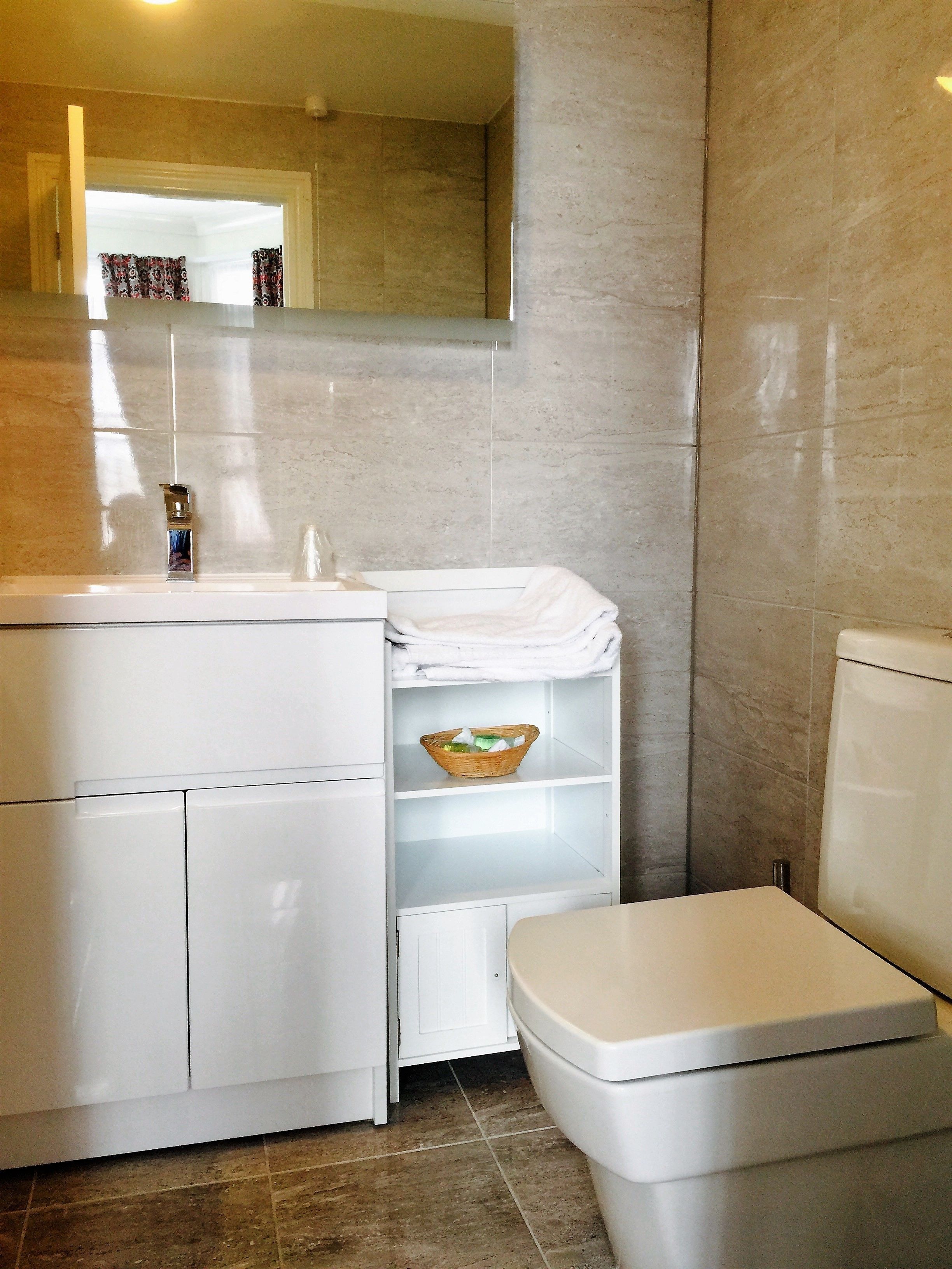 A bathroom with a white vanity, a mirror, a toilet, and a shelf with towels and a basket.