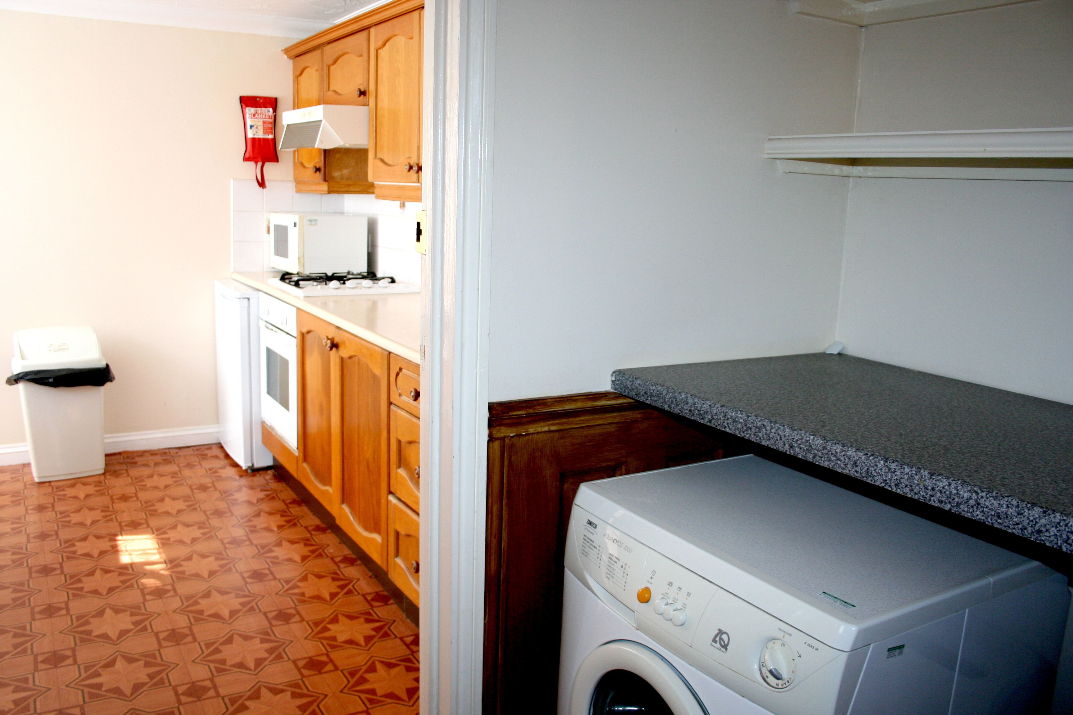 A laundry room with a washing machine, a microwave, and wooden cabinets.