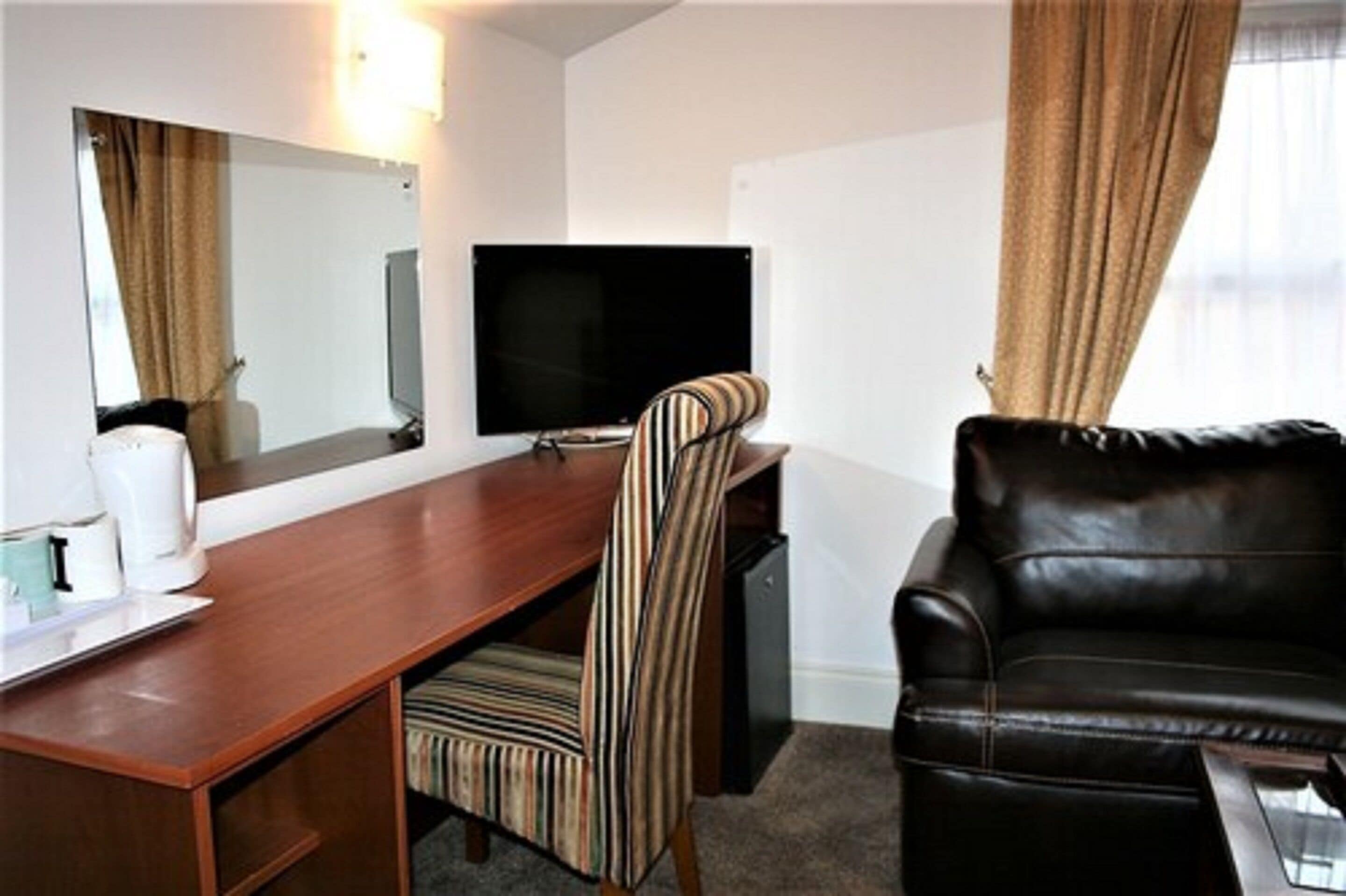 A hotel room with a wooden desk, a television, a striped chair, and a black leather sofa.