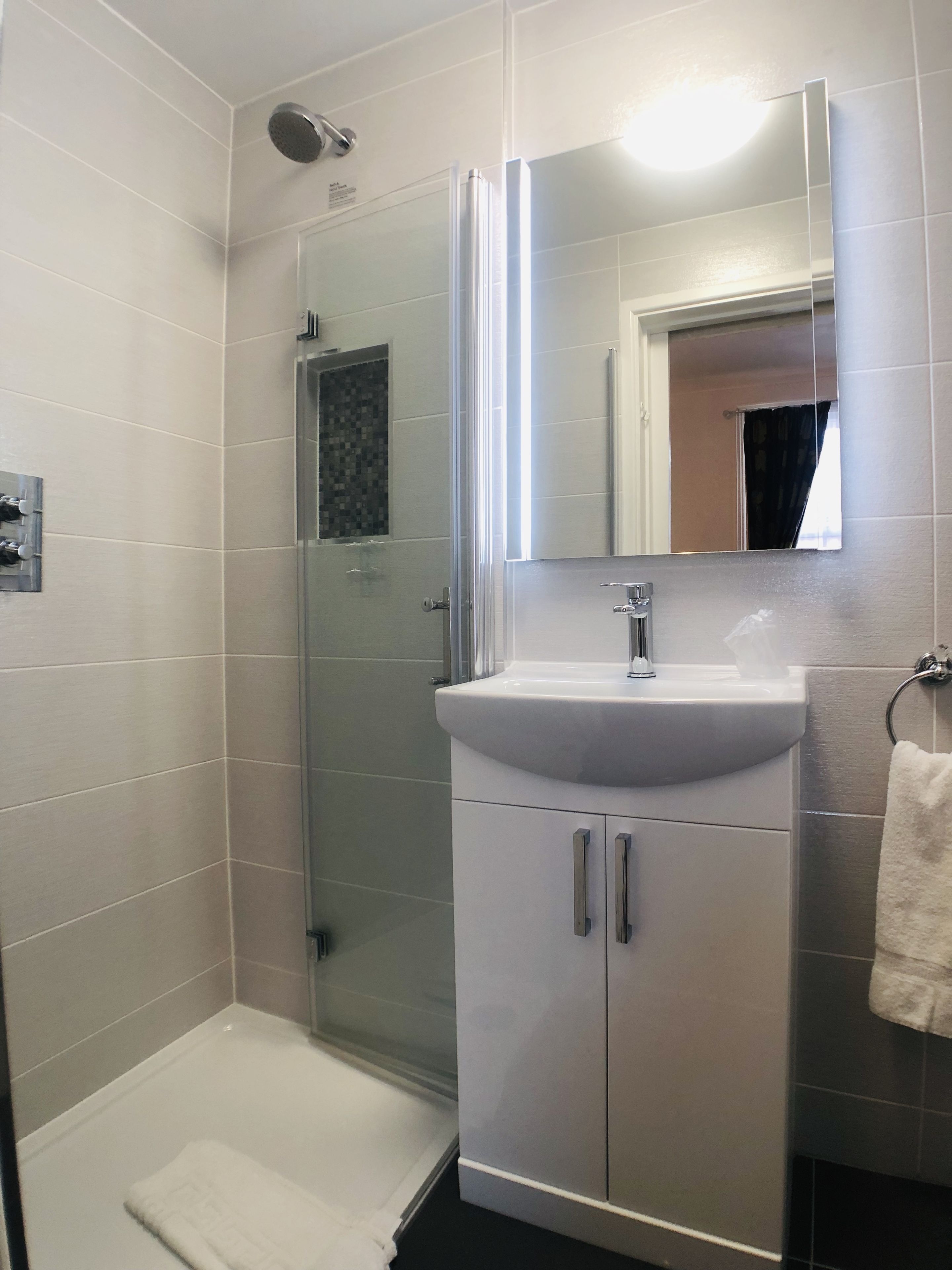 A modern bathroom with a glass-enclosed shower, a white sink, and a mirror above it.